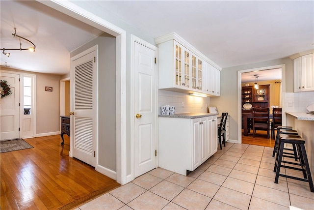 kitchen with tasteful backsplash, white cabinets, glass insert cabinets, and light tile patterned flooring