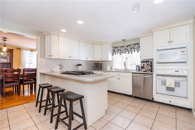 kitchen featuring a breakfast bar area, light countertops, light tile patterned floors, white appliances, and white cabinetry