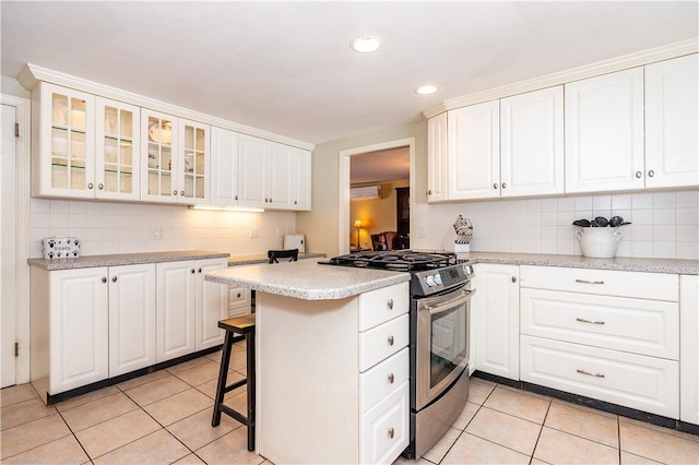 kitchen with light countertops, light tile patterned flooring, stainless steel range with gas stovetop, and backsplash