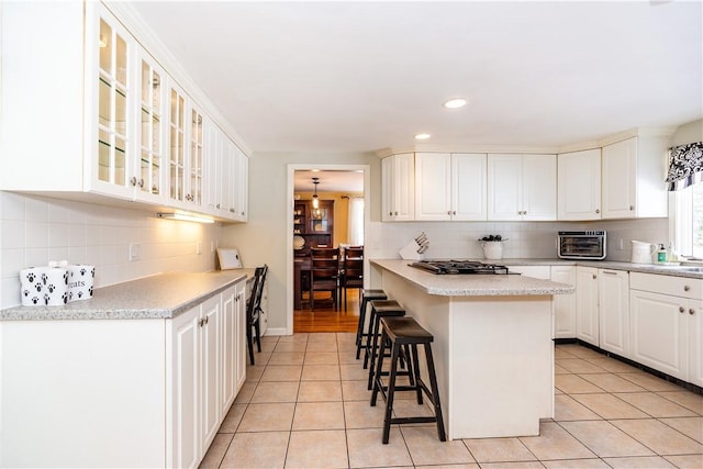 kitchen featuring light tile patterned flooring, a kitchen breakfast bar, glass insert cabinets, and light countertops