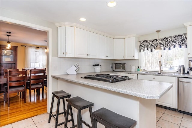 kitchen featuring gas cooktop, white cabinetry, a breakfast bar, a sink, and dishwasher