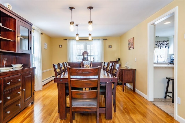 dining space featuring a baseboard heating unit, light wood-type flooring, and baseboards