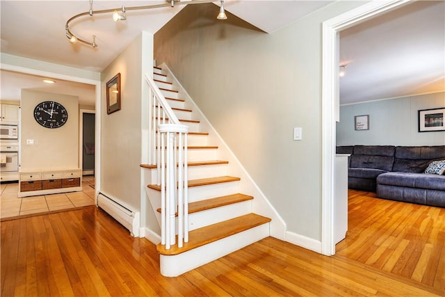 stairway featuring a baseboard radiator, baseboards, hardwood / wood-style floors, and rail lighting