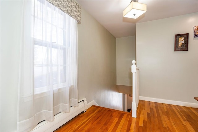 unfurnished bedroom with wood finished floors, baseboards, and baseboard heating