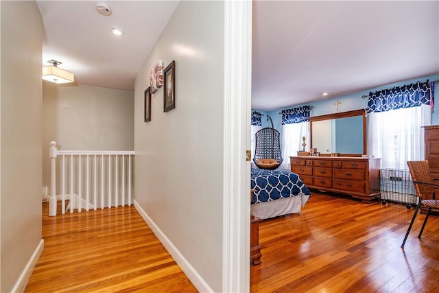 corridor with an upstairs landing, wood finished floors, and baseboards