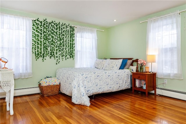 bedroom with multiple windows, wood finished floors, and a baseboard radiator