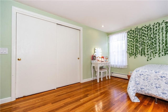 bedroom with wood finished floors, baseboards, a closet, and a baseboard radiator