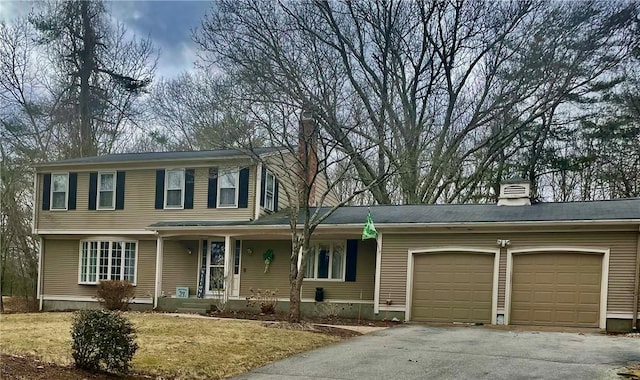 view of front facade with a porch, an attached garage, driveway, and a chimney