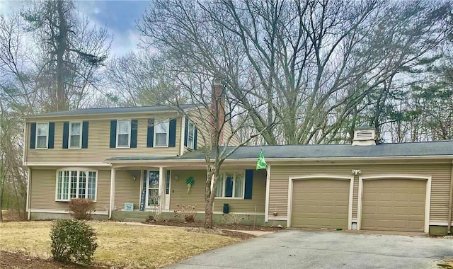 view of front of house featuring an attached garage, a chimney, covered porch, and driveway