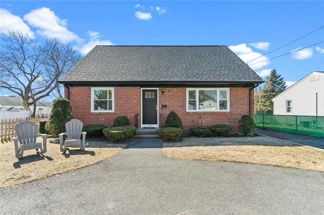 view of front of home with brick siding, a shingled roof, and fence