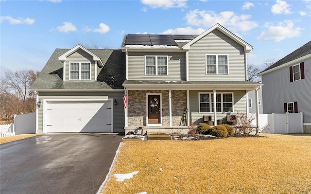 traditional home with fence, a porch, stone siding, aphalt driveway, and roof mounted solar panels