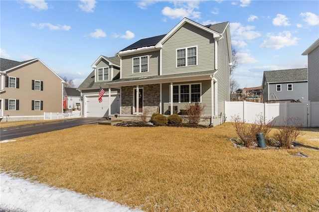 traditional-style house with a front yard, fence, driveway, covered porch, and stone siding