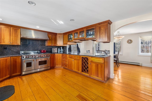 kitchen with range with two ovens, wall chimney range hood, a baseboard heating unit, arched walkways, and a sink