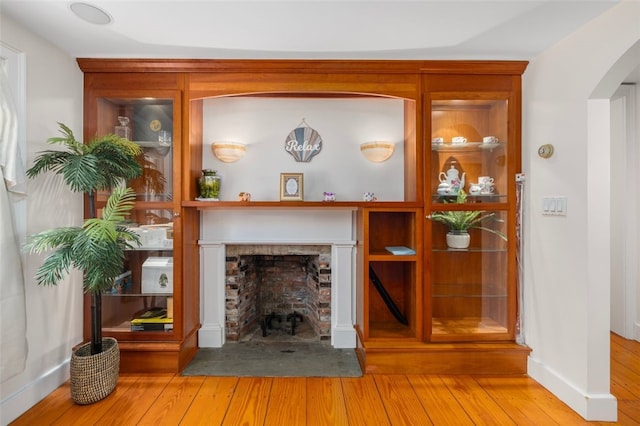 living area featuring wood finished floors, a fireplace with flush hearth, arched walkways, and baseboards