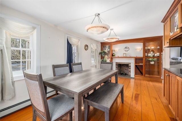 dining space featuring a baseboard radiator, a fireplace, and light wood-style floors