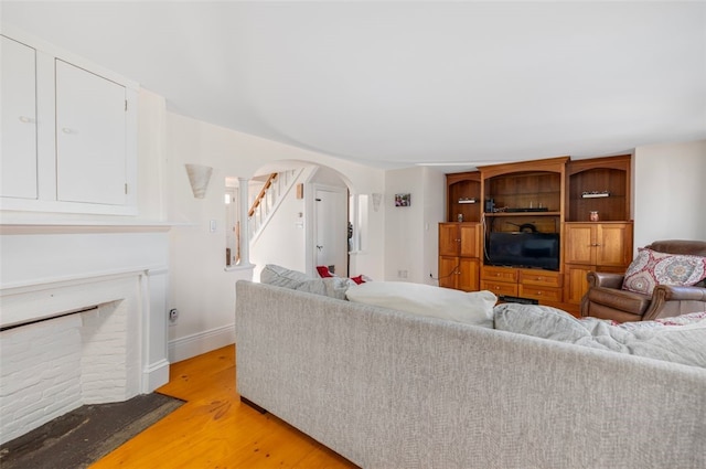 living area featuring arched walkways, light wood-style floors, stairway, and baseboards