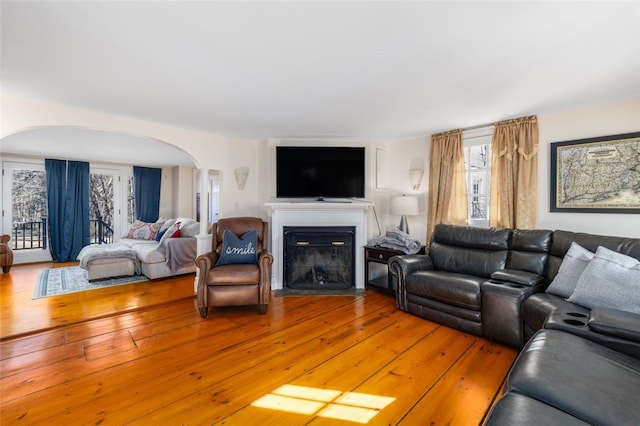 living room featuring arched walkways, a fireplace with flush hearth, and light wood finished floors