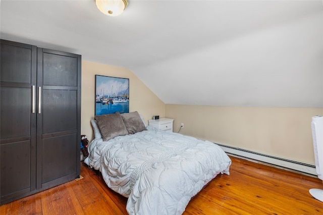 bedroom with a baseboard heating unit, vaulted ceiling, and hardwood / wood-style flooring