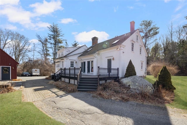 view of side of property featuring a chimney, a deck, and asphalt driveway