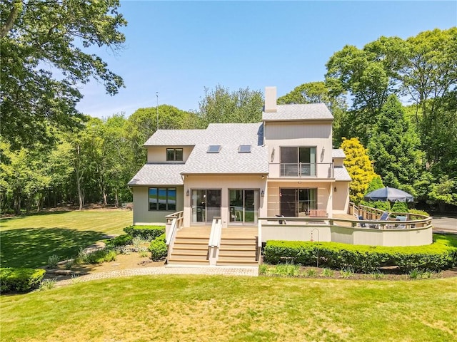 back of house featuring a balcony, a chimney, stairs, a shingled roof, and a lawn