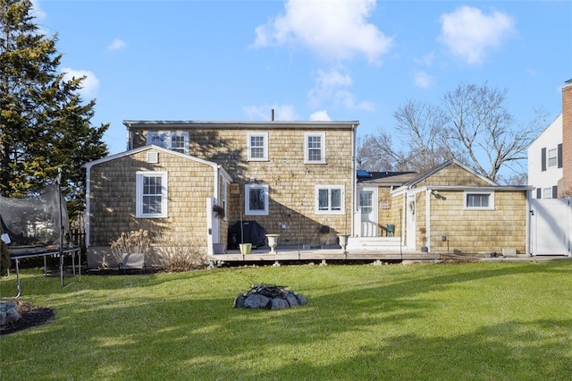 rear view of property featuring a deck, a trampoline, and a lawn