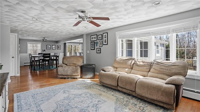 living room featuring ceiling fan, baseboard heating, wood finished floors, and a textured ceiling