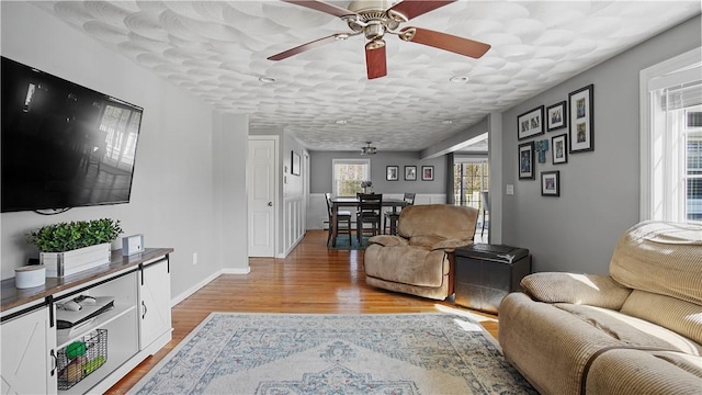 living area featuring light wood finished floors, baseboards, and ceiling fan