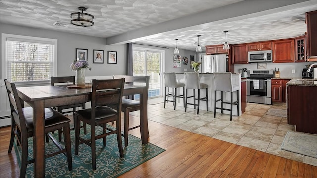 dining room with light wood-style flooring, visible vents, and a textured ceiling