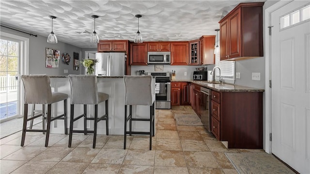 kitchen featuring dark stone countertops, a breakfast bar area, a sink, stainless steel appliances, and decorative light fixtures