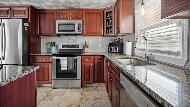 kitchen with glass insert cabinets, light stone countertops, appliances with stainless steel finishes, and a sink