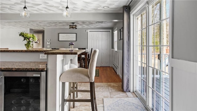 interior space featuring wine cooler, baseboard heating, wainscoting, and hanging light fixtures