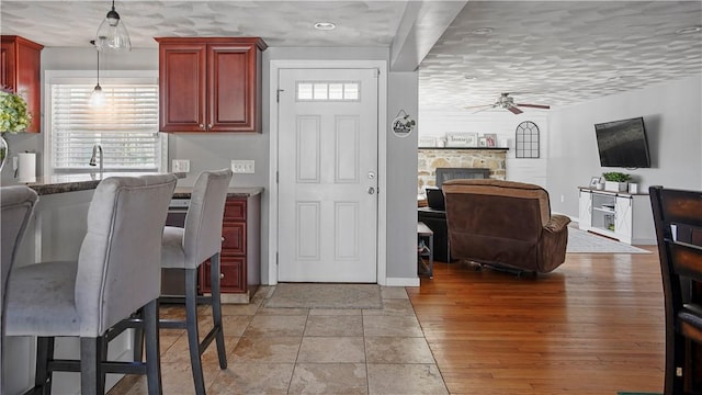 kitchen featuring light wood-type flooring, a ceiling fan, open floor plan, a stone fireplace, and dark brown cabinets