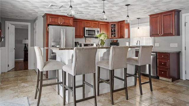 kitchen featuring visible vents, stainless steel appliances, glass insert cabinets, pendant lighting, and a kitchen bar