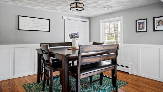 dining space with a decorative wall, wainscoting, and wood finished floors