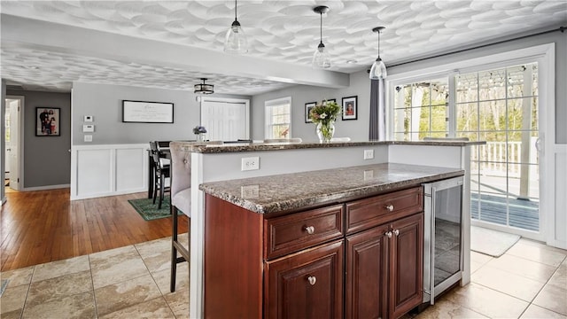 kitchen featuring a kitchen island, wine cooler, dark stone countertops, a kitchen breakfast bar, and hanging light fixtures