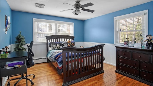 bedroom with a baseboard radiator, visible vents, light wood finished floors, and wainscoting