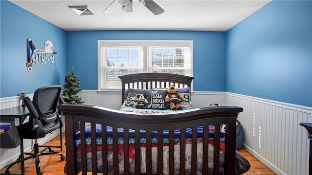 bedroom with visible vents, wainscoting, a ceiling fan, and wood finished floors