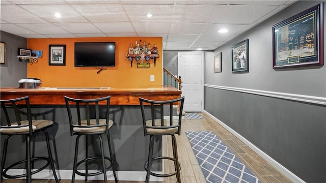 bar featuring wood finished floors, baseboards, recessed lighting, a drop ceiling, and a bar