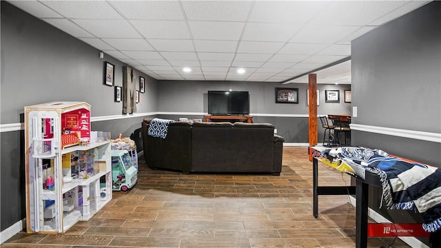 living area with a drop ceiling, recessed lighting, baseboards, and wood finish floors