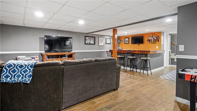 living area featuring bar area, wood finished floors, stairway, baseboards, and a paneled ceiling