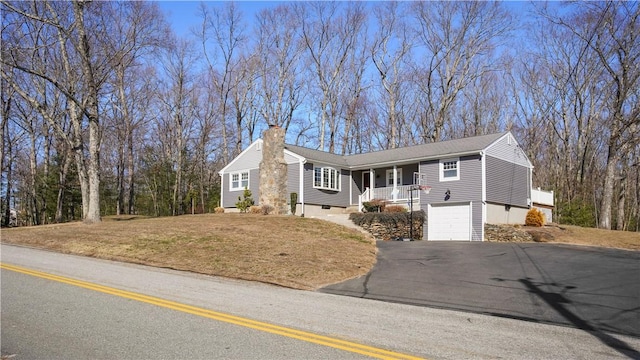 single story home with a garage, covered porch, a chimney, and aphalt driveway