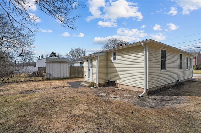 rear view of house with fence, a chimney, entry steps, an outdoor structure, and a storage unit