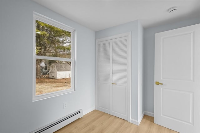 unfurnished bedroom featuring light wood-style flooring, baseboards, a closet, and baseboard heating