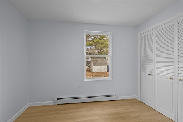 unfurnished bedroom with a closet, light wood finished floors, baseboards, and baseboard heating