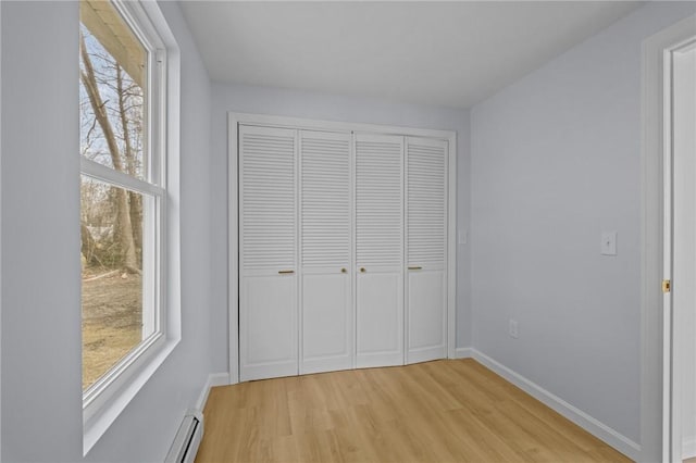 unfurnished bedroom with light wood-style flooring, multiple windows, baseboards, and a closet