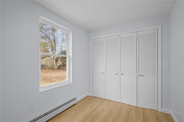 unfurnished bedroom featuring a closet, baseboards, a baseboard heating unit, and light wood-style floors