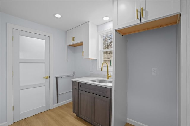 kitchen with light wood-type flooring, light countertops, recessed lighting, white cabinets, and a sink