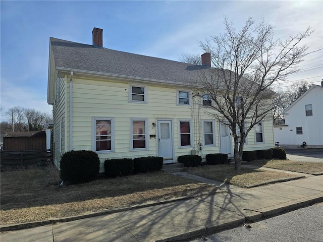 colonial home with a chimney and roof with shingles