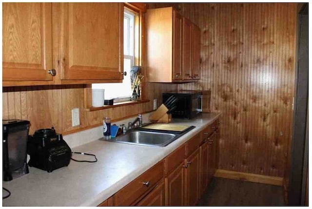 kitchen with a sink, wood walls, brown cabinetry, black microwave, and light countertops