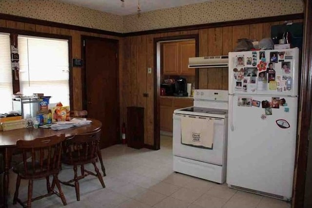 kitchen featuring white appliances, wooden walls, light countertops, under cabinet range hood, and brown cabinets